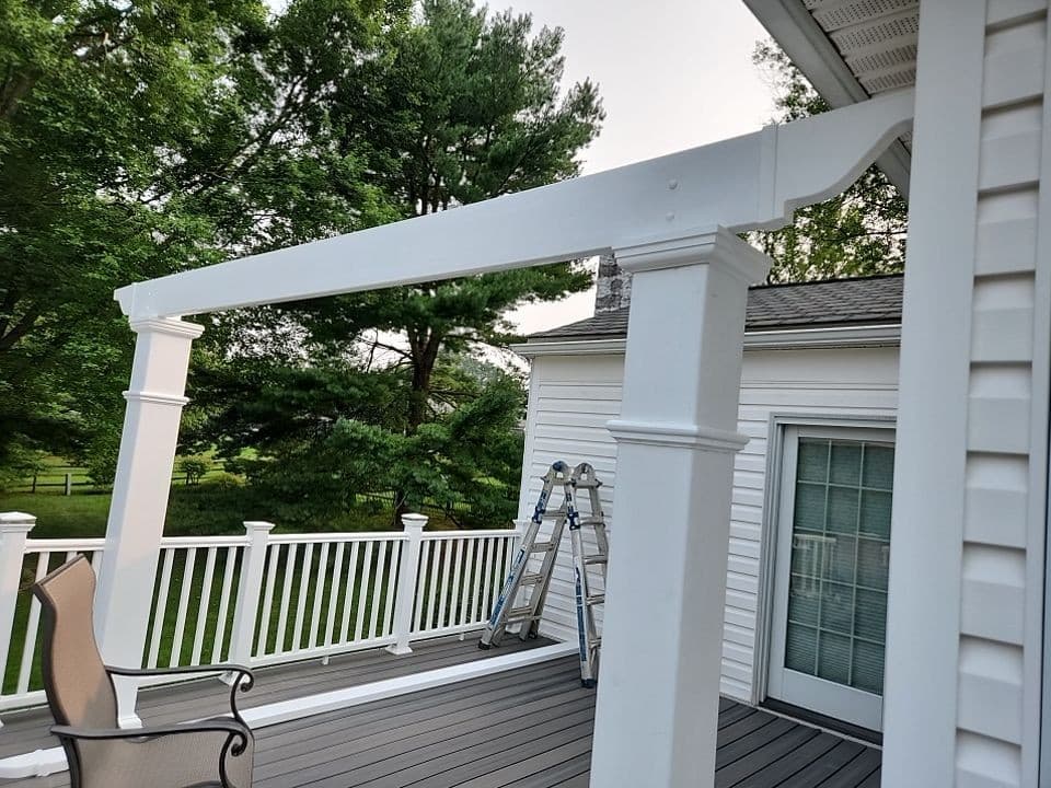 White vinyl attached pergola with substantial columns and a beam over a composite deck with white railings, attached to a home.