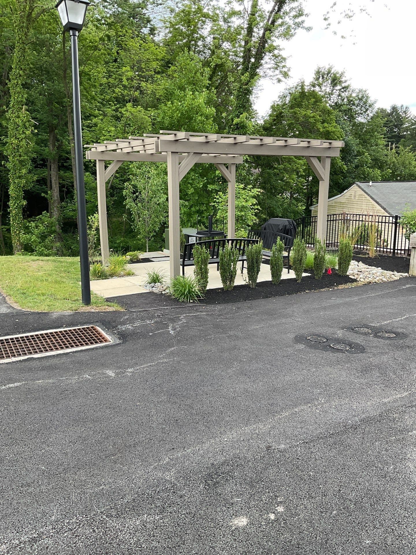 Freestanding tan cedar pergola with bench seating and ornamental grasses in a landscaped community courtyard.
