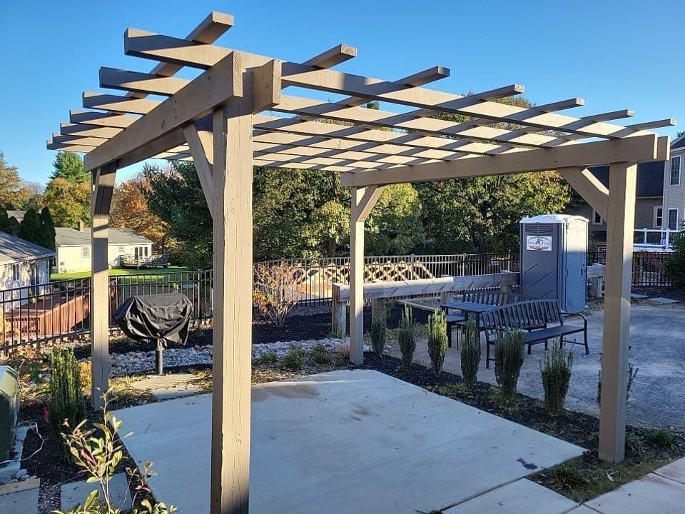 Freestanding cedar pergola with decorative rafter tails and a lattice top over a concrete patio in a fenced backyard.