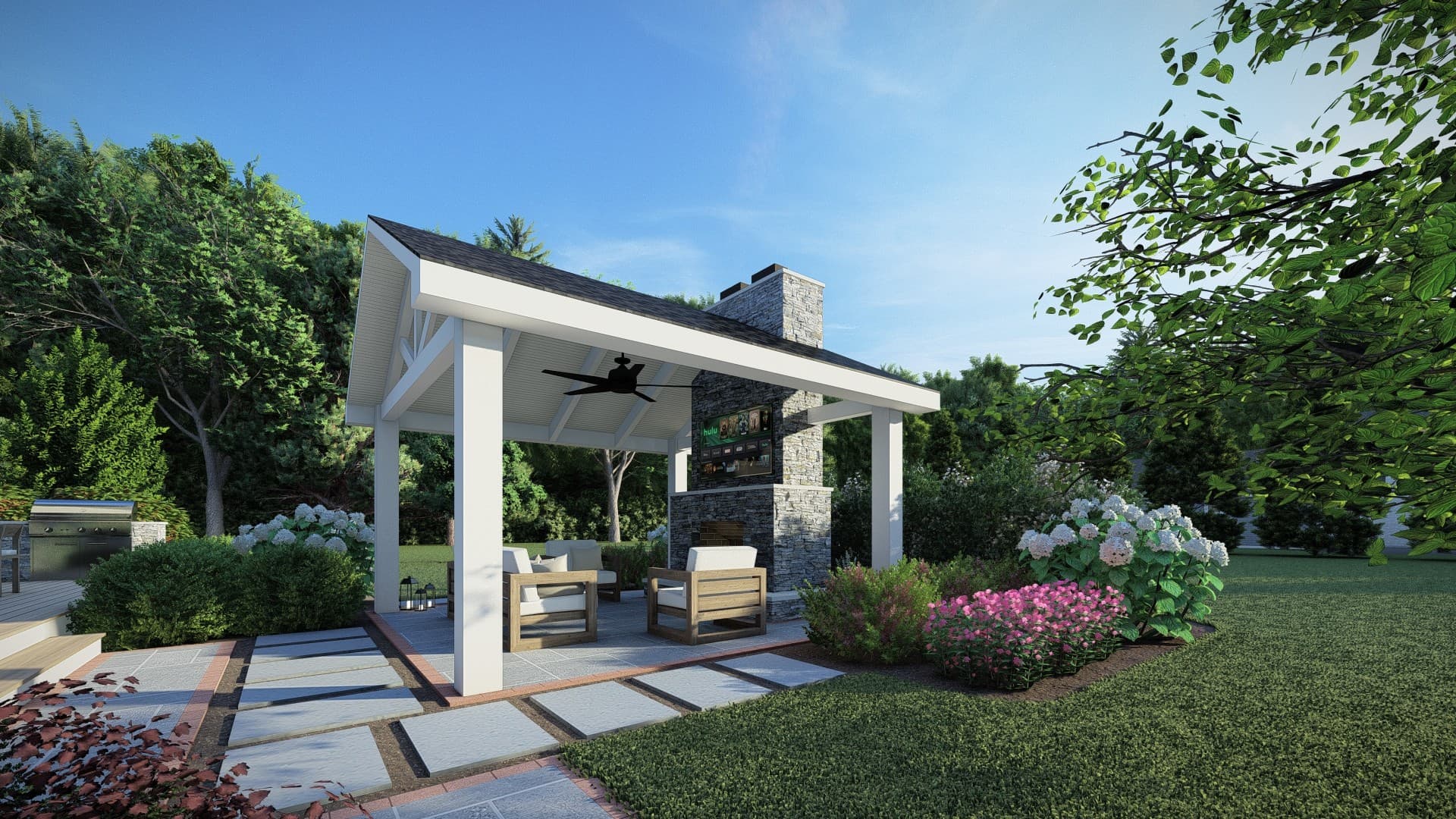White timber pavilion with a stone outdoor fireplace, ceiling fan, and cushioned lounge seating on a bluestone paver patio framed by hydrangeas, built by JHL Pergolas.