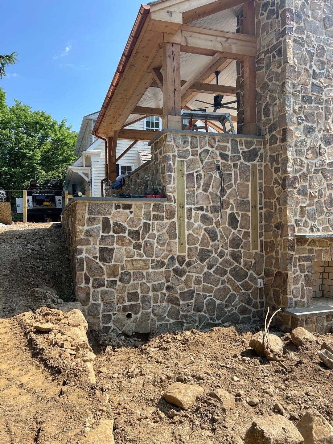 Stone-veneer half-wall and column detail of a cedar timber-frame pavilion, showing the fieldstone masonry base and cedar posts.